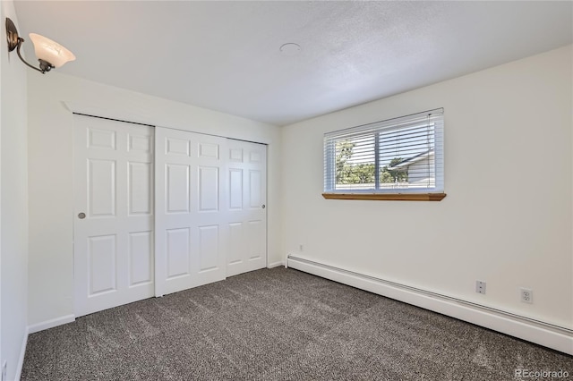 unfurnished bedroom featuring baseboards, a baseboard radiator, dark carpet, and a closet