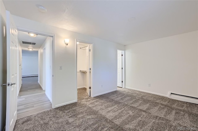 unfurnished bedroom featuring visible vents, a baseboard radiator, a walk in closet, baseboard heating, and carpet flooring