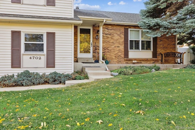 entrance to property featuring brick siding, a lawn, and a shingled roof