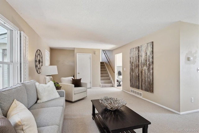 living area with baseboards, visible vents, stairs, a textured ceiling, and light carpet