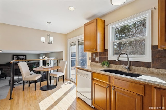 kitchen with brown cabinets, a sink, backsplash, light wood-style floors, and dishwasher