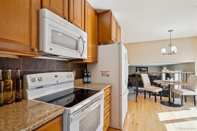 kitchen with pendant lighting, decorative backsplash, brown cabinets, light wood-style floors, and white appliances