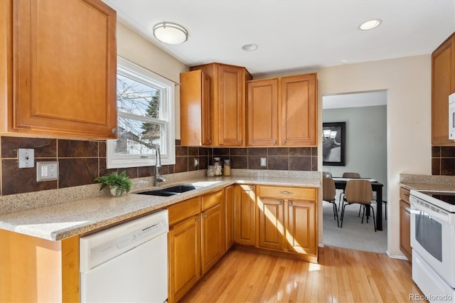 kitchen featuring a sink, tasteful backsplash, white appliances, light wood finished floors, and light stone countertops