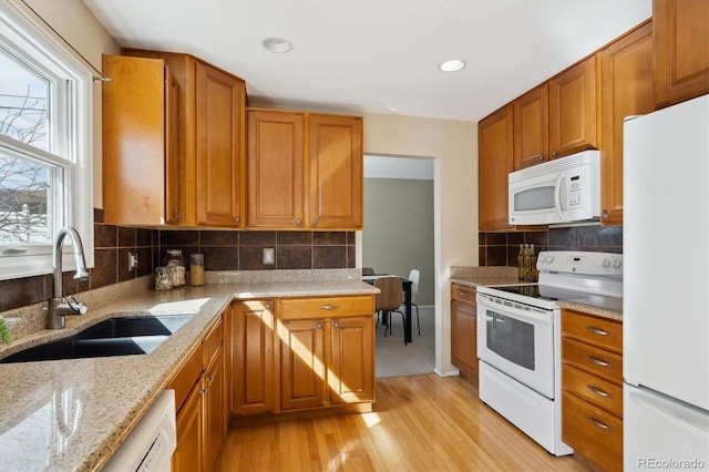 kitchen with light stone countertops, light wood-style flooring, brown cabinetry, white appliances, and a sink