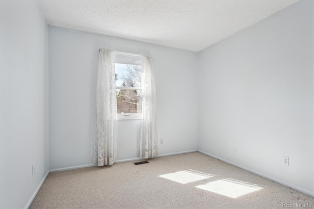 carpeted spare room with visible vents, baseboards, and a textured ceiling