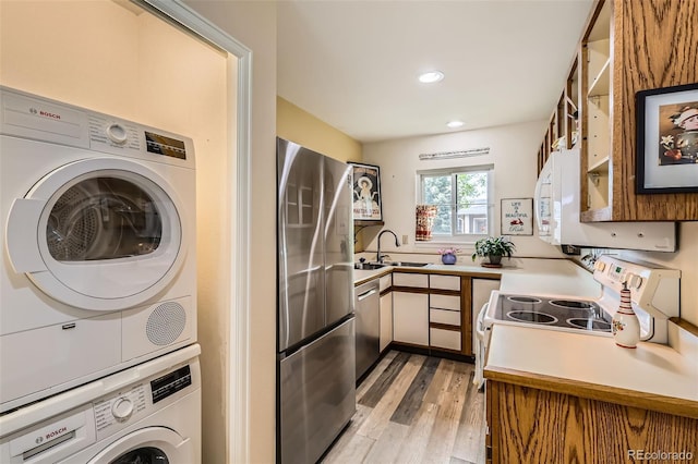 kitchen with stacked washer / drying machine, a sink, light countertops, light wood-style flooring, and stainless steel appliances