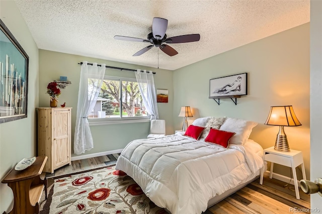 bedroom with a textured ceiling, baseboards, a ceiling fan, and wood finished floors