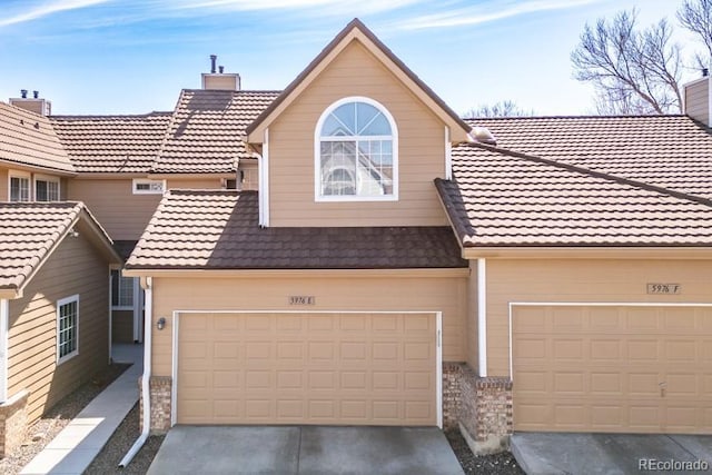 multi unit property featuring concrete driveway, a tile roof, and a chimney