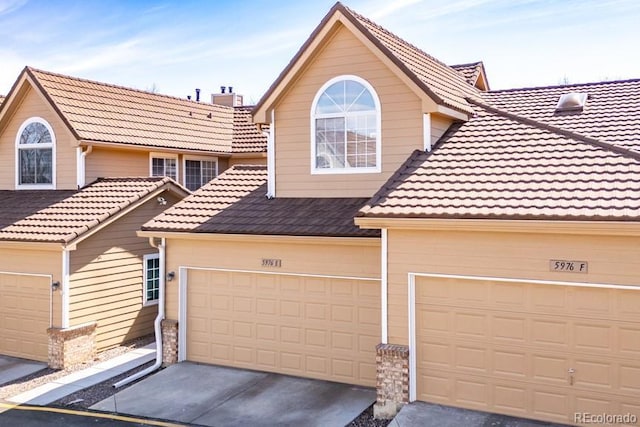 townhome / multi-family property with a tiled roof, concrete driveway, a chimney, and an attached garage