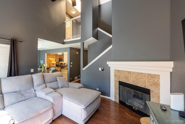 living area featuring a tile fireplace, a towering ceiling, baseboards, and wood finished floors