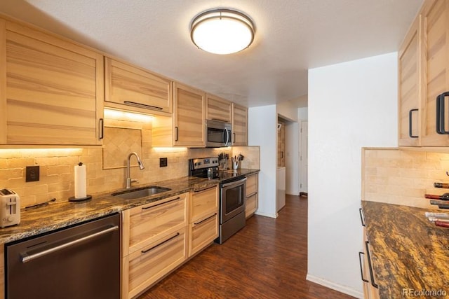 kitchen with dark wood-style floors, light brown cabinetry, appliances with stainless steel finishes, a sink, and dark stone counters