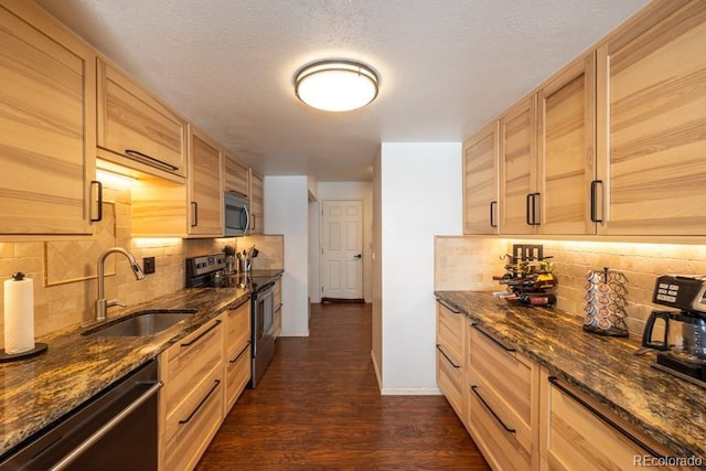 kitchen featuring appliances with stainless steel finishes, dark wood-type flooring, a sink, dark stone counters, and baseboards