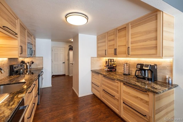 kitchen with stainless steel appliances, a sink, baseboards, backsplash, and dark wood finished floors