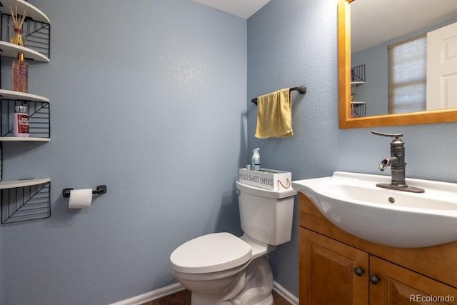 half bathroom with a textured wall, vanity, toilet, and baseboards