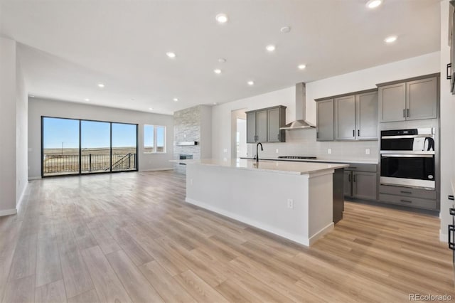 kitchen featuring light wood-type flooring, gray cabinets, wall chimney range hood, light countertops, and decorative backsplash