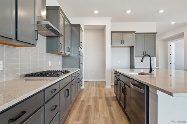 kitchen featuring light stone counters, appliances with stainless steel finishes, wall chimney exhaust hood, and a sink