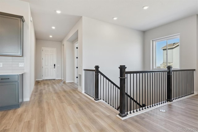 hall with an upstairs landing, recessed lighting, light wood-type flooring, and baseboards