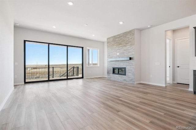 unfurnished living room featuring recessed lighting, a stone fireplace, light wood-style flooring, and baseboards