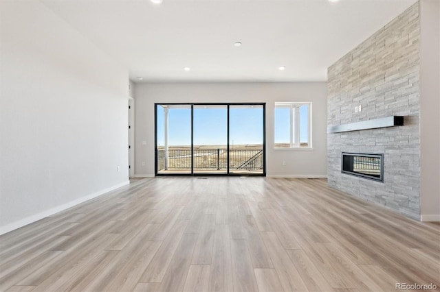 unfurnished living room featuring baseboards, a stone fireplace, and light wood-style flooring