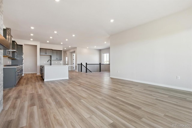 unfurnished living room with light wood finished floors, recessed lighting, baseboards, and a sink