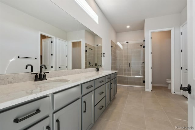 bathroom with double vanity, a sink, tile patterned flooring, a shower stall, and toilet