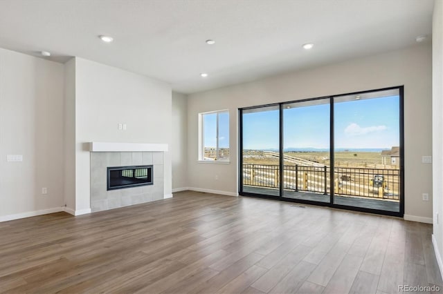 unfurnished living room with baseboards, wood finished floors, recessed lighting, and a tile fireplace