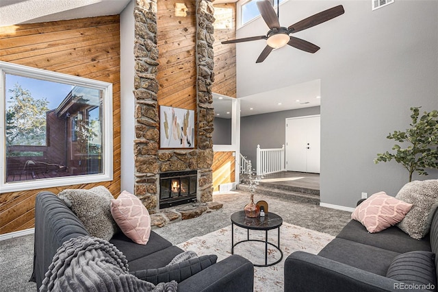 carpeted living room featuring high vaulted ceiling, a fireplace, ceiling fan, and wooden walls