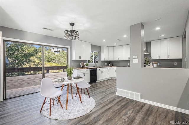 kitchen featuring wall chimney range hood, black dishwasher, white cabinetry, and hardwood / wood-style flooring