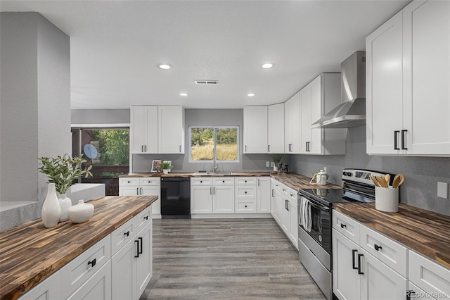 kitchen with wall chimney range hood, light hardwood / wood-style floors, butcher block counters, stainless steel electric range oven, and dishwasher