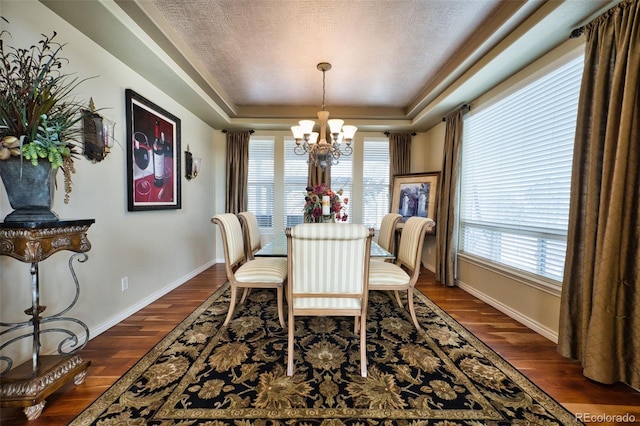 dining space with dark hardwood / wood-style floors, a textured ceiling, a chandelier, and a tray ceiling