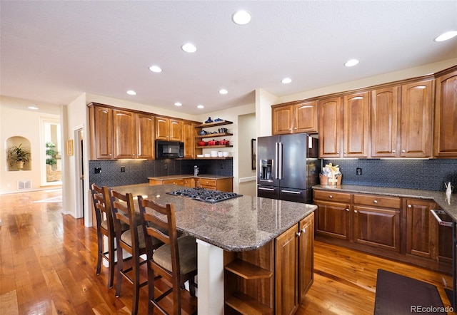 kitchen with black microwave, high quality fridge, a kitchen island, open shelves, and stovetop