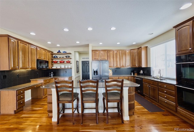 kitchen featuring sink, a kitchen island, black appliances, a kitchen bar, and dark hardwood / wood-style flooring