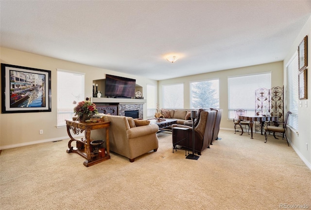 living room featuring light carpet, a stone fireplace, a textured ceiling, and a healthy amount of sunlight