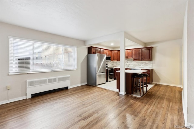 kitchen featuring a kitchen bar, light hardwood / wood-style flooring, radiator, stainless steel appliances, and decorative backsplash