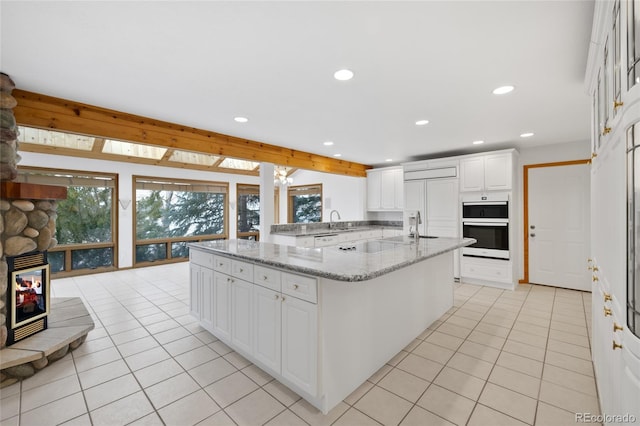 kitchen featuring kitchen peninsula, light tile patterned floors, light stone counters, cooktop, and white cabinetry