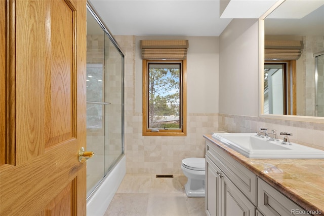 full bathroom featuring vanity, toilet, tile walls, and enclosed tub / shower combo