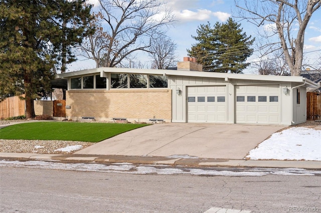 mid-century modern home with a fenced front yard, brick siding, a chimney, an attached garage, and driveway