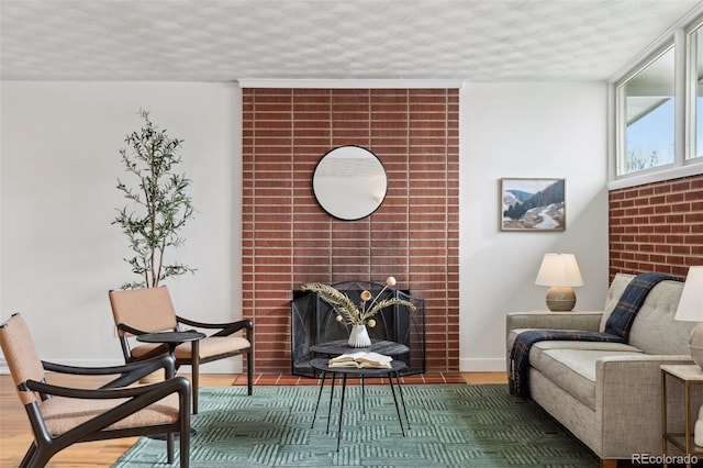 sitting room with a textured ceiling, a brick fireplace, wood finished floors, and baseboards