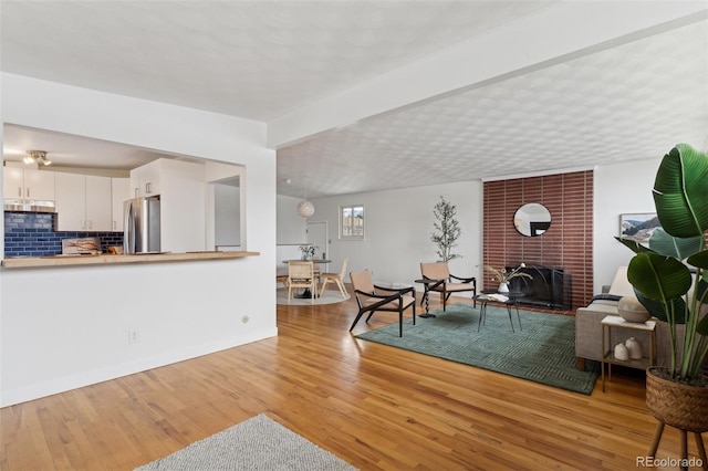 living room with a brick fireplace, light wood-style flooring, and baseboards