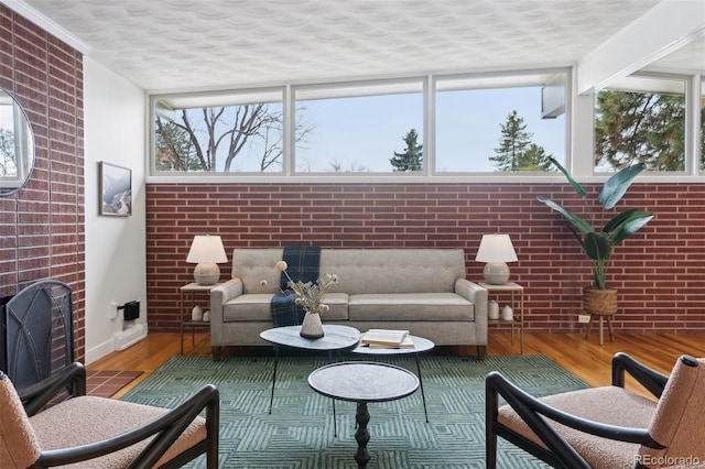 living area featuring a textured ceiling, brick wall, a fireplace, and wood finished floors