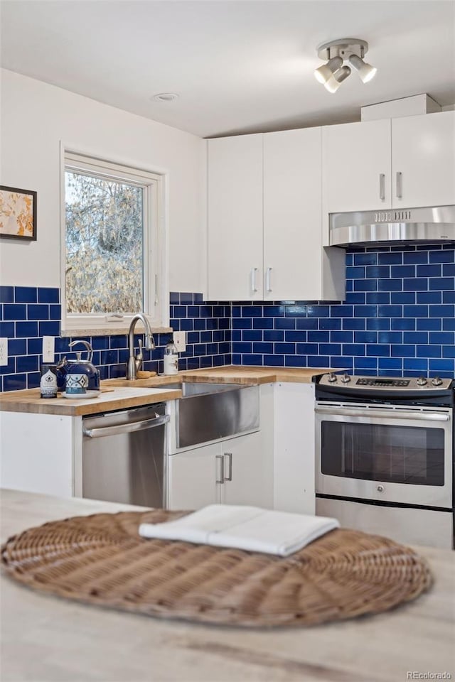 kitchen featuring under cabinet range hood, stainless steel appliances, white cabinets, wooden counters, and decorative backsplash