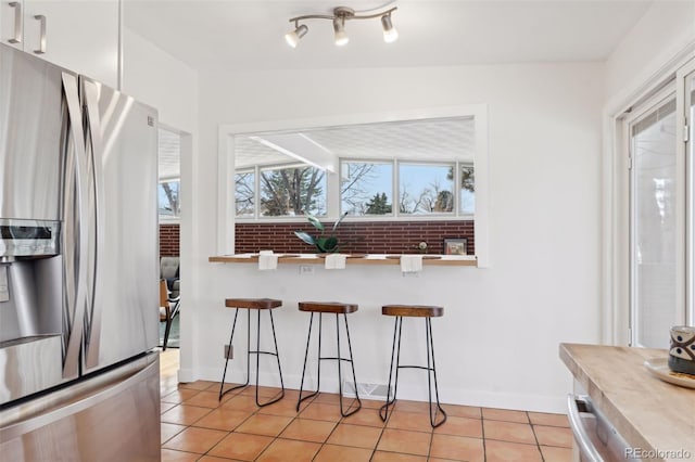 kitchen with light tile patterned floors, baseboards, stainless steel fridge with ice dispenser, a kitchen breakfast bar, and light countertops