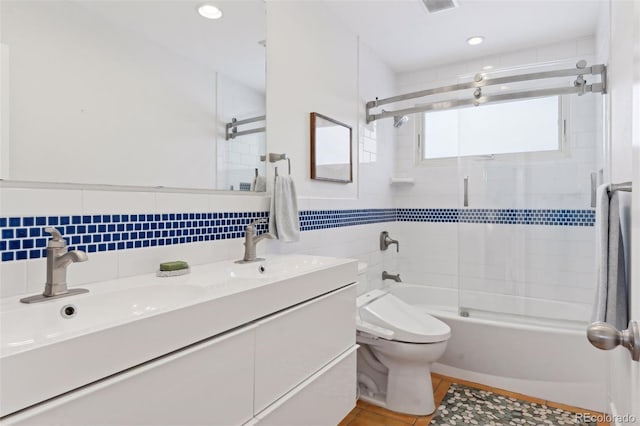 bathroom with double vanity, bath / shower combo with glass door, toilet, a sink, and tile walls