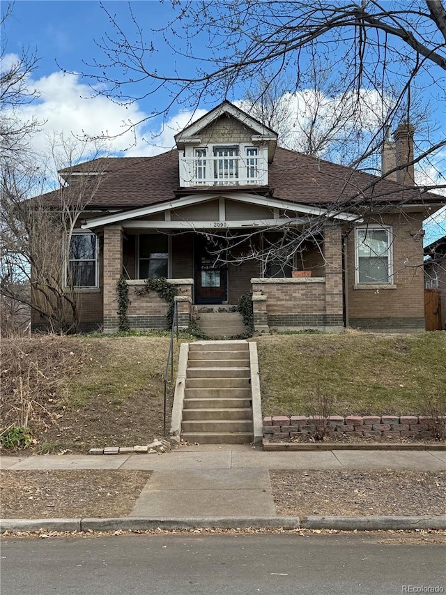 view of front of house featuring a shingled roof, covered porch, a front lawn, and a chimney