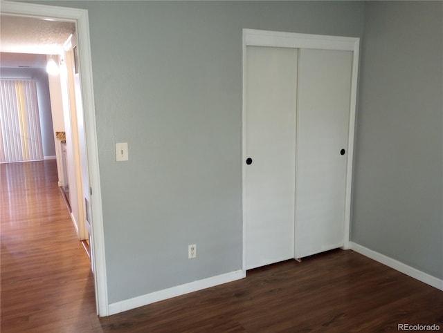 unfurnished bedroom with dark wood-style floors, baseboards, and a closet
