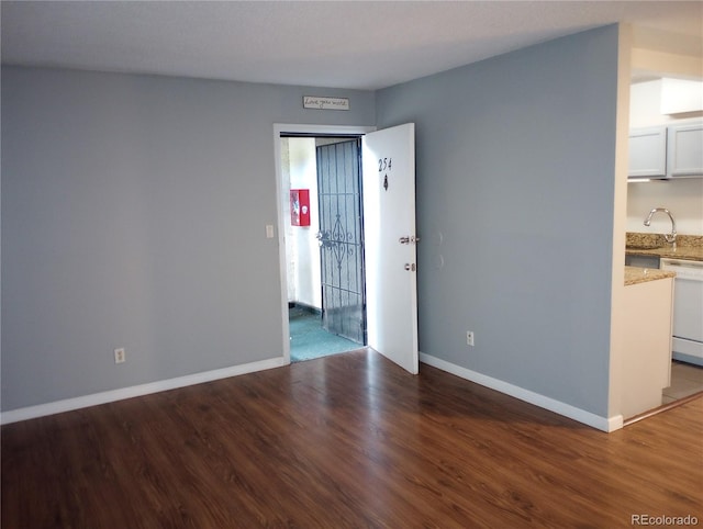 spare room featuring wood finished floors, a sink, and baseboards