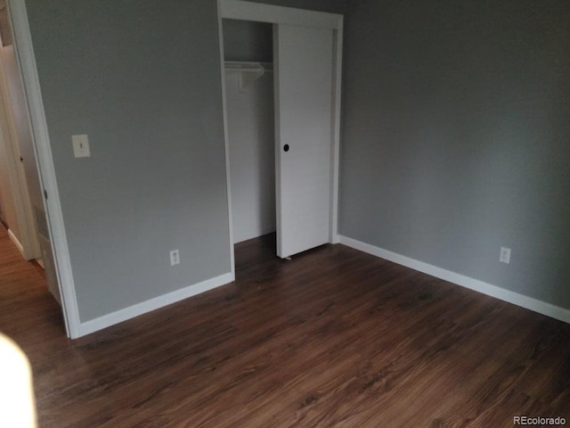 unfurnished bedroom with baseboards, dark wood finished floors, and a closet