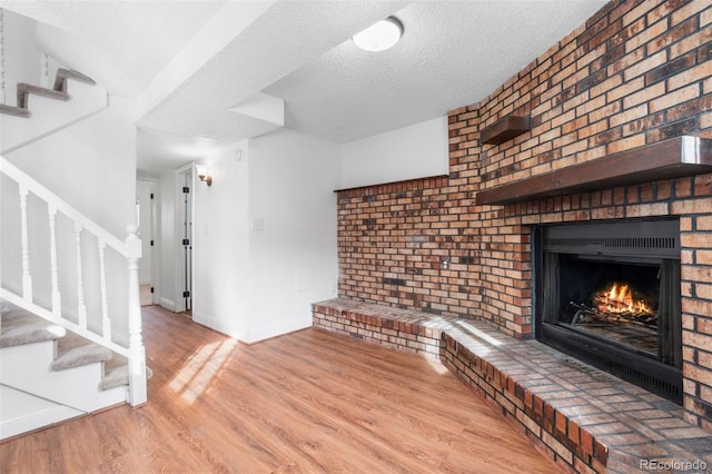 unfurnished living room featuring baseboards, stairway, wood finished floors, a textured ceiling, and a brick fireplace