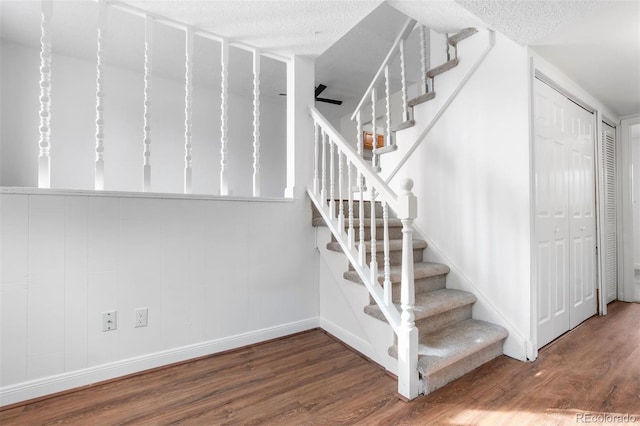 stairs with a textured ceiling, wood finished floors, and baseboards