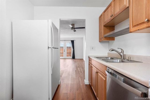 kitchen with dishwasher, wood finished floors, freestanding refrigerator, light countertops, and a sink